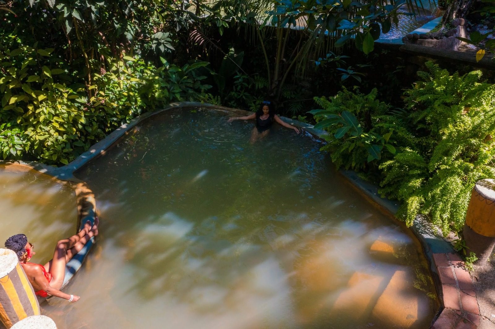 Guests relaxing in warm mineral pools shaded by rainforest plants